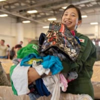 両手いっぱいの衣類に笑顔の女性自衛官（画像：USAF）