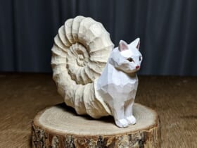 神の使いか妖怪か……猫と化石が融合したアンモニャイトの木彫り作品